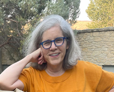 Mujer con cabello entrecano, gafas y blusa color calabaza. Mark Medzadourian Hughes, crédito de la foto.